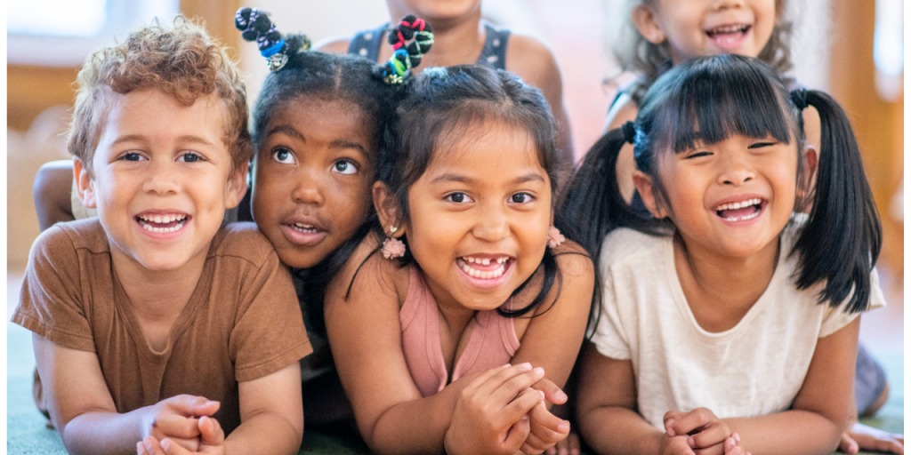 Group of smiling children laying together, belly first on the floor